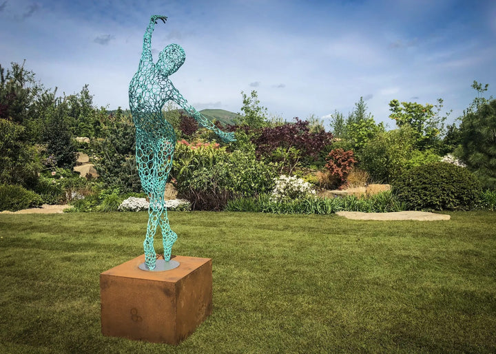 Simon Gudgeon bronze sculpture Athena featuring an elegant open lattice female form with blue green patina displayed within a landscaped outdoor garden setting.