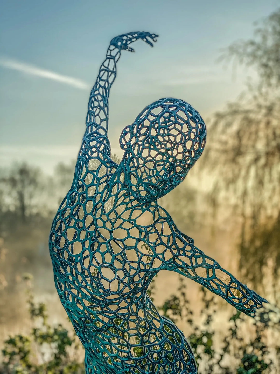 Simon Gudgeon bronze sculpture Athena featuring an elegant open lattice female form with blue green patina displayed within a landscaped outdoor garden setting.
