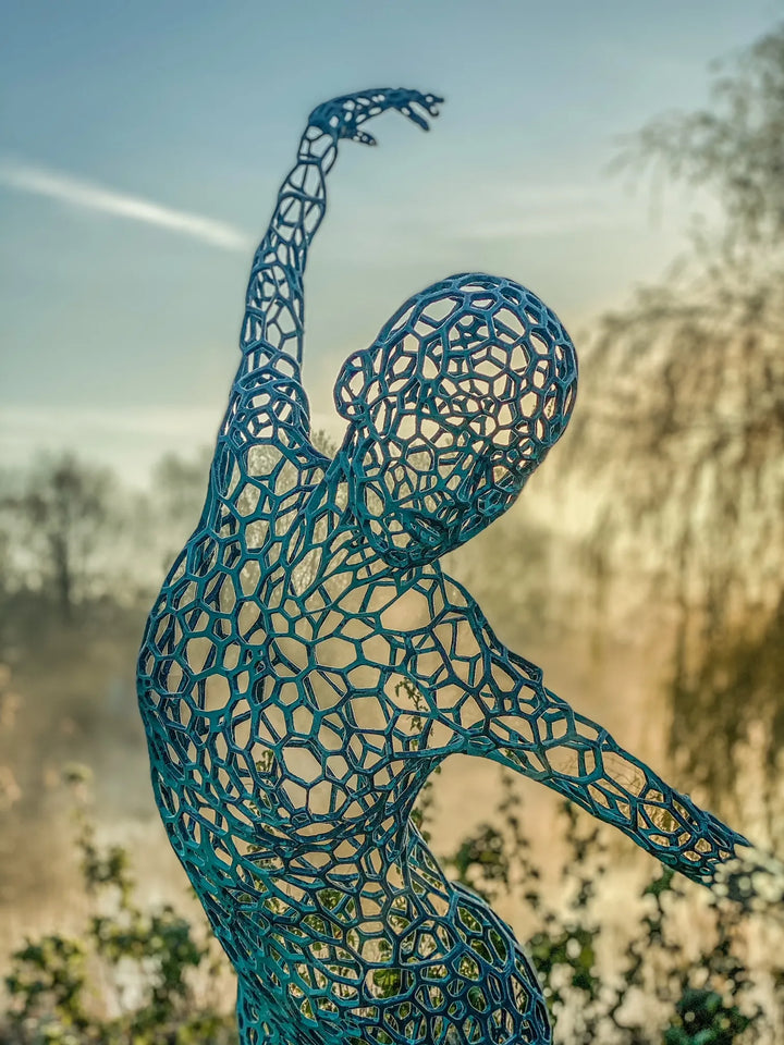 Simon Gudgeon bronze sculpture Athena featuring an elegant open lattice female form with blue green patina displayed within a landscaped outdoor garden setting.