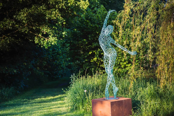 Simon Gudgeon bronze sculpture Athena featuring an elegant open lattice female form with blue green patina displayed within a landscaped outdoor garden setting.