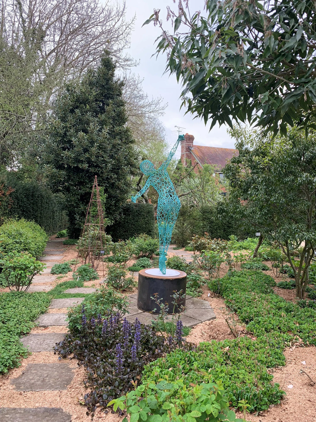 Simon Gudgeon bronze sculpture Athena featuring an elegant open lattice female form with blue green patina displayed within a landscaped outdoor garden setting.