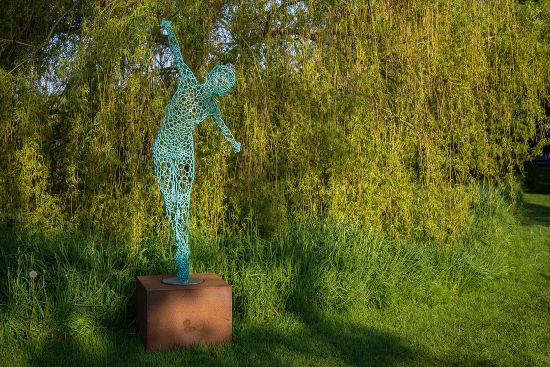 Simon Gudgeon bronze sculpture Athena featuring an elegant open lattice female form with blue green patina displayed within a landscaped outdoor garden setting.
