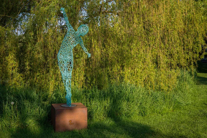 Simon Gudgeon bronze sculpture Athena featuring an elegant open lattice female form with blue green patina displayed within a landscaped outdoor garden setting.