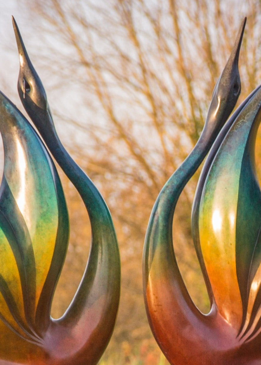 Simon Gudgeon bronze sculpture Dancing Cranes featuring elegant crane-inspired organic forms with sweeping upward curves displayed within a landscaped garden setting.