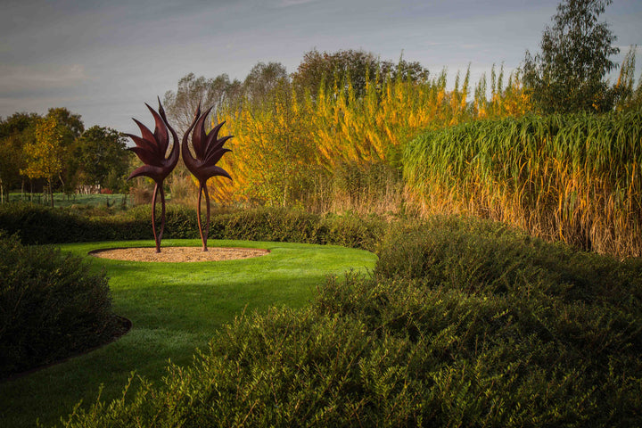 Simon Gudgeon bronze sculpture Dancing Cranes featuring elegant crane-inspired organic forms with sweeping upward curves displayed within a landscaped garden setting.