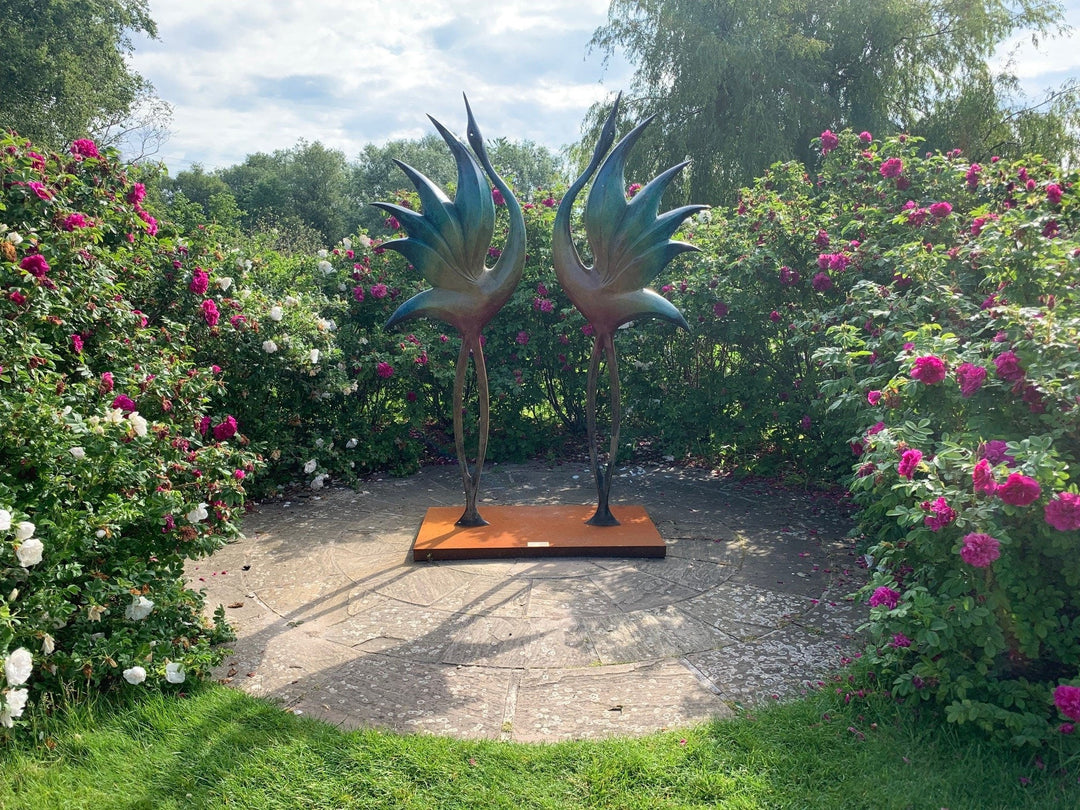 Simon Gudgeon bronze sculpture Dancing Cranes featuring elegant crane-inspired organic forms with sweeping upward curves displayed within a landscaped garden setting.