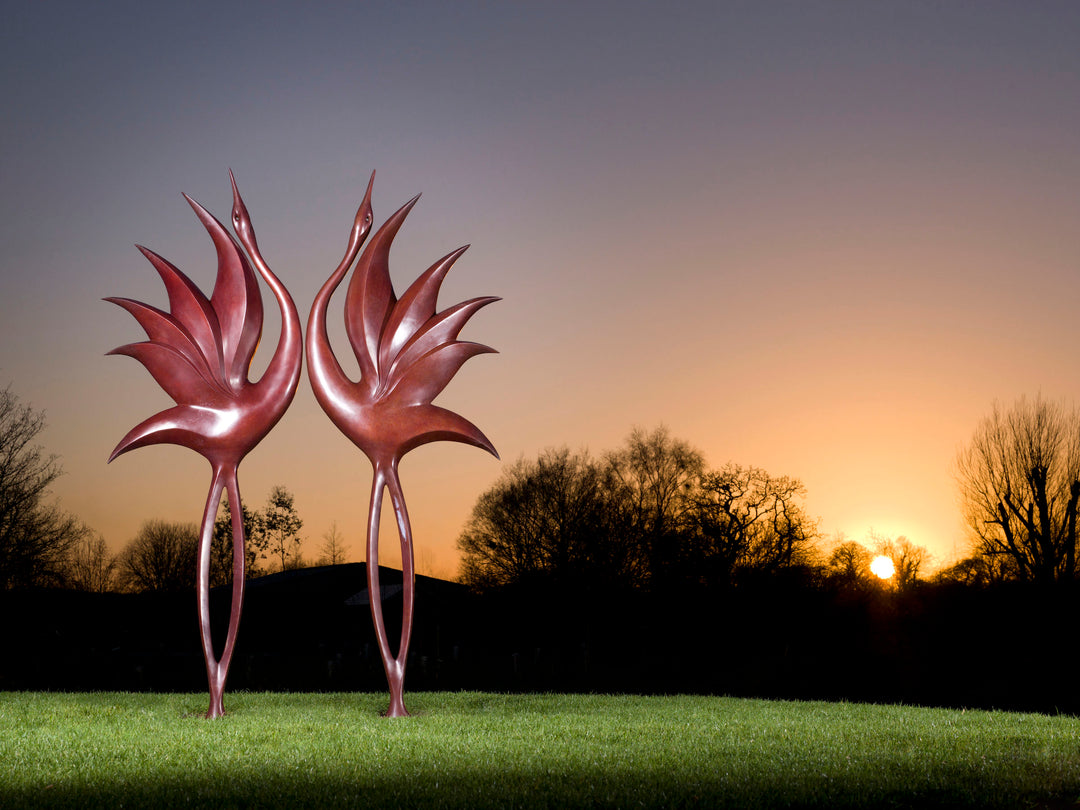 Simon Gudgeon bronze sculpture Dancing Cranes featuring elegant crane-inspired organic forms with sweeping upward curves displayed within a landscaped garden setting.
