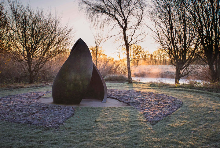 Simon Gudgeon bronze sculpture Embrace featuring monumental abstract curved bronze forms rising upwards and meeting at a central point within a landscaped garden setting.
