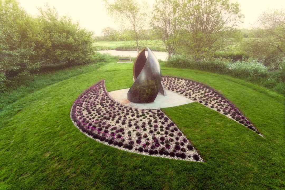 Simon Gudgeon bronze sculpture Embrace featuring monumental abstract curved bronze forms rising upwards and meeting at a central point within a landscaped garden setting.
