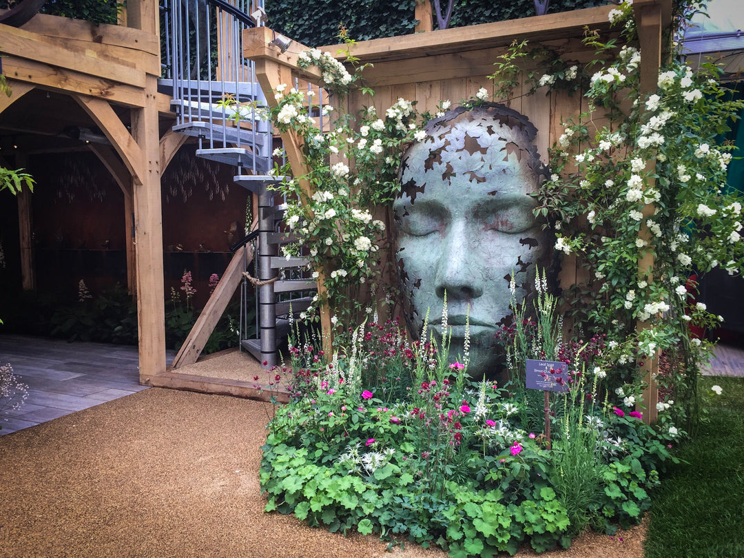 Simon Gudgeon bronze sculpture Leaf Spirit featuring a serene monumental face formed with organic leaf patterns displayed within a landscaped garden and woodland setting.
