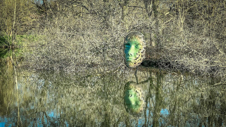 Simon Gudgeon bronze sculpture Leaf Spirit featuring a serene monumental face formed with organic leaf patterns displayed within a landscaped garden and woodland setting.