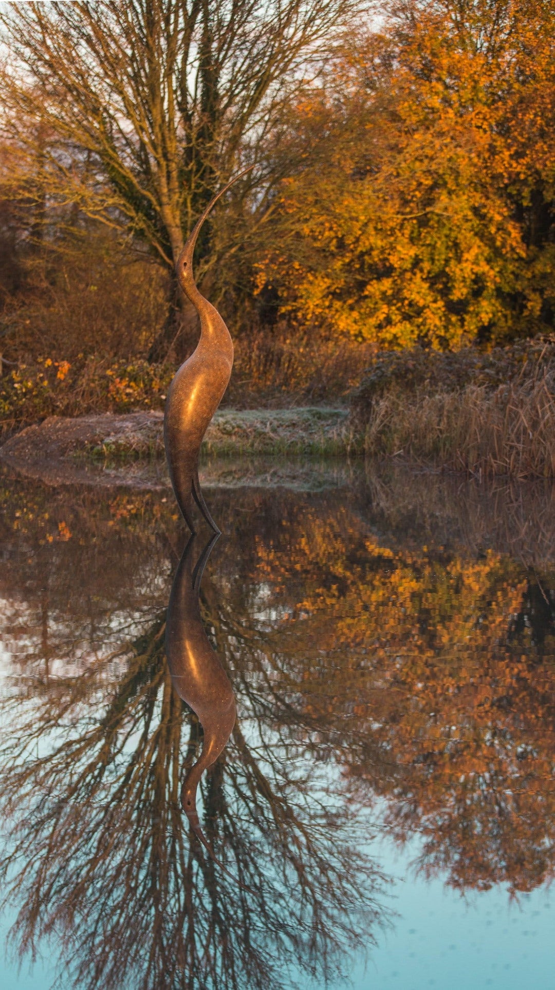 Simon Gudgeon bronze sculpture Origins featuring a tall abstract organic bird-inspired form with elegant flowing curves displayed within a landscaped outdoor setting.