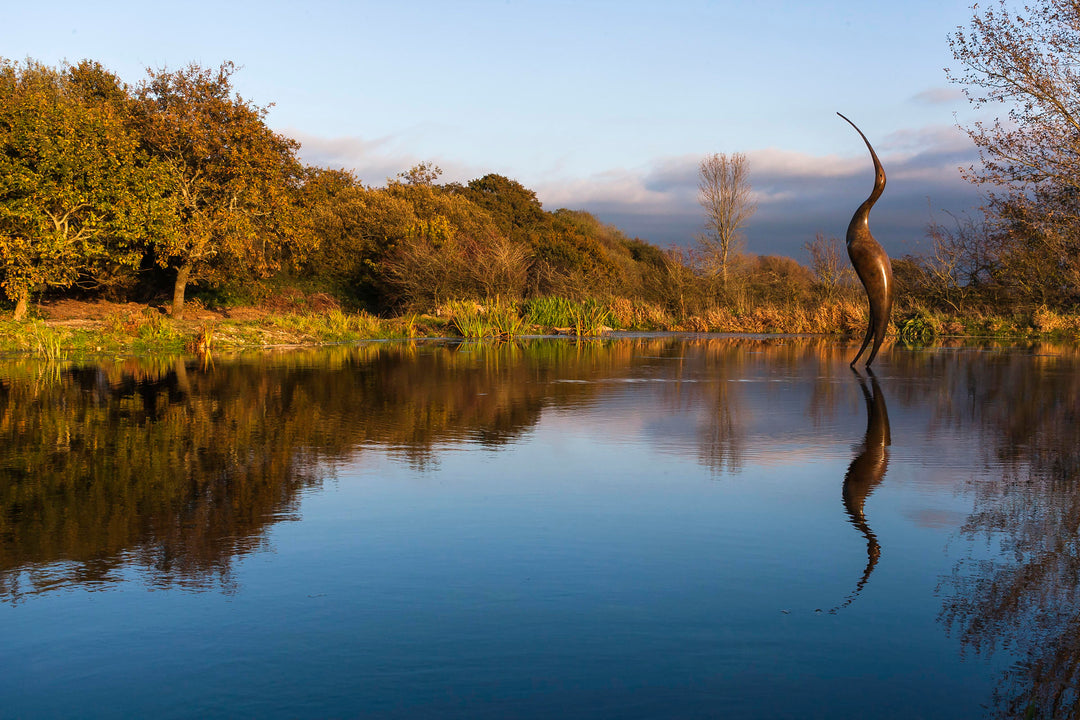 Simon Gudgeon bronze sculpture Origins featuring a tall abstract organic bird-inspired form with elegant flowing curves displayed within a landscaped outdoor setting.