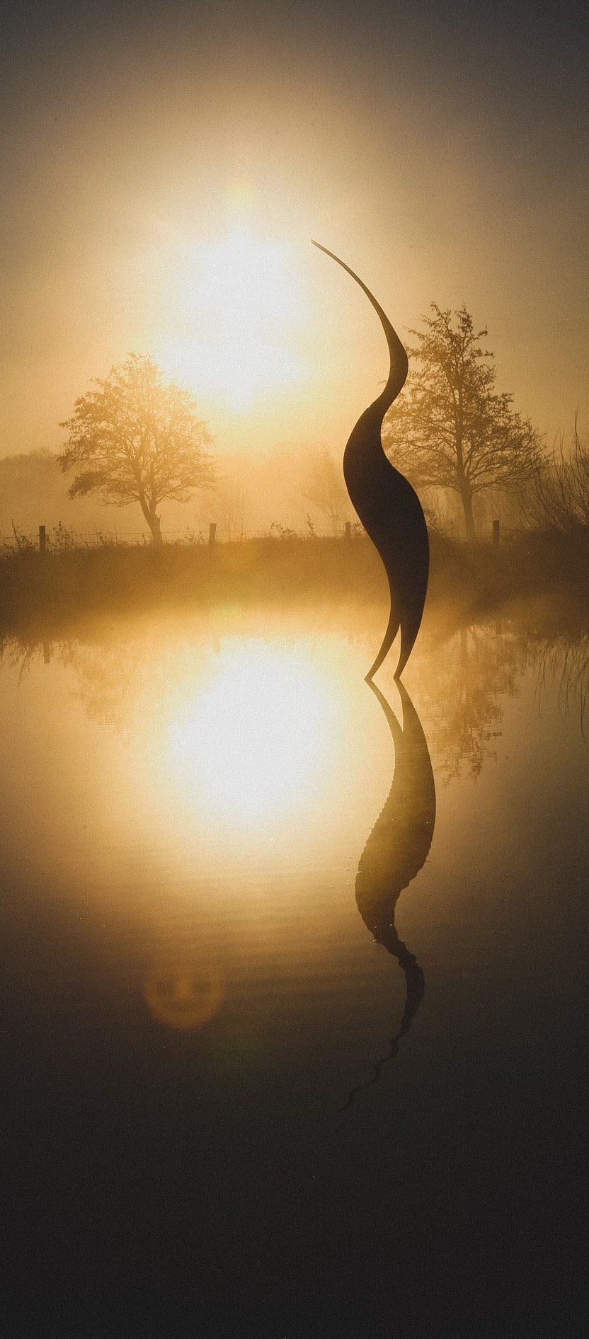 Simon Gudgeon bronze sculpture Origins featuring a tall abstract organic bird-inspired form with elegant flowing curves displayed within a landscaped outdoor setting.