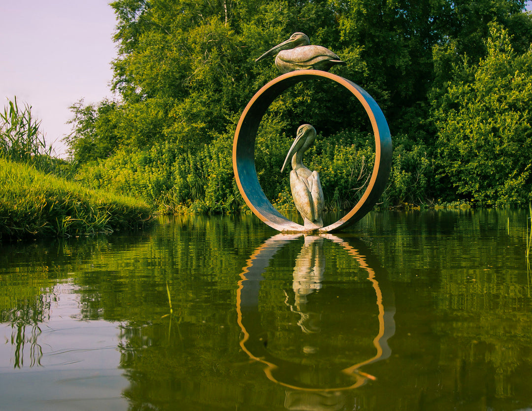Simon Gudgeon bronze sculpture Pelicans featuring two elegant stylised pelican forms positioned around a circular contemporary bronze structure within a landscaped outdoor setting.