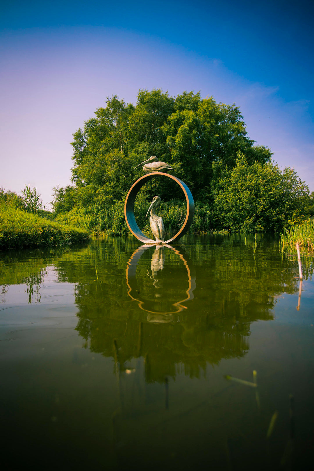 Simon Gudgeon bronze sculpture Pelicans featuring two elegant stylised pelican forms positioned around a circular contemporary bronze structure within a landscaped outdoor setting.