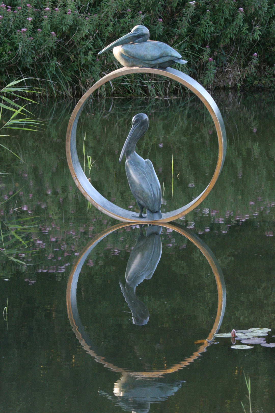 Simon Gudgeon bronze sculpture Pelicans featuring two elegant stylised pelican forms positioned around a circular contemporary bronze structure within a landscaped outdoor setting.