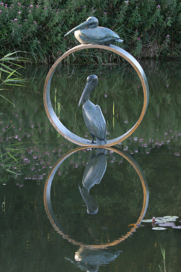 Simon Gudgeon bronze sculpture Pelicans featuring two elegant stylised pelican forms positioned around a circular contemporary bronze structure within a landscaped outdoor setting.