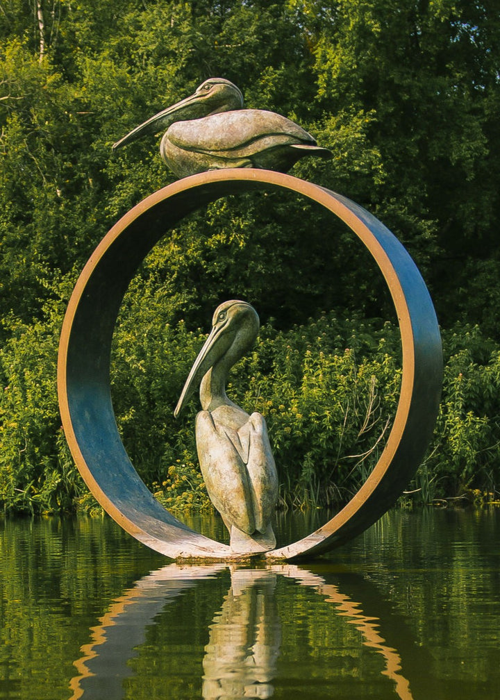 Simon Gudgeon bronze sculpture Pelicans featuring two elegant stylised pelican forms positioned around a circular contemporary bronze structure within a landscaped outdoor setting.