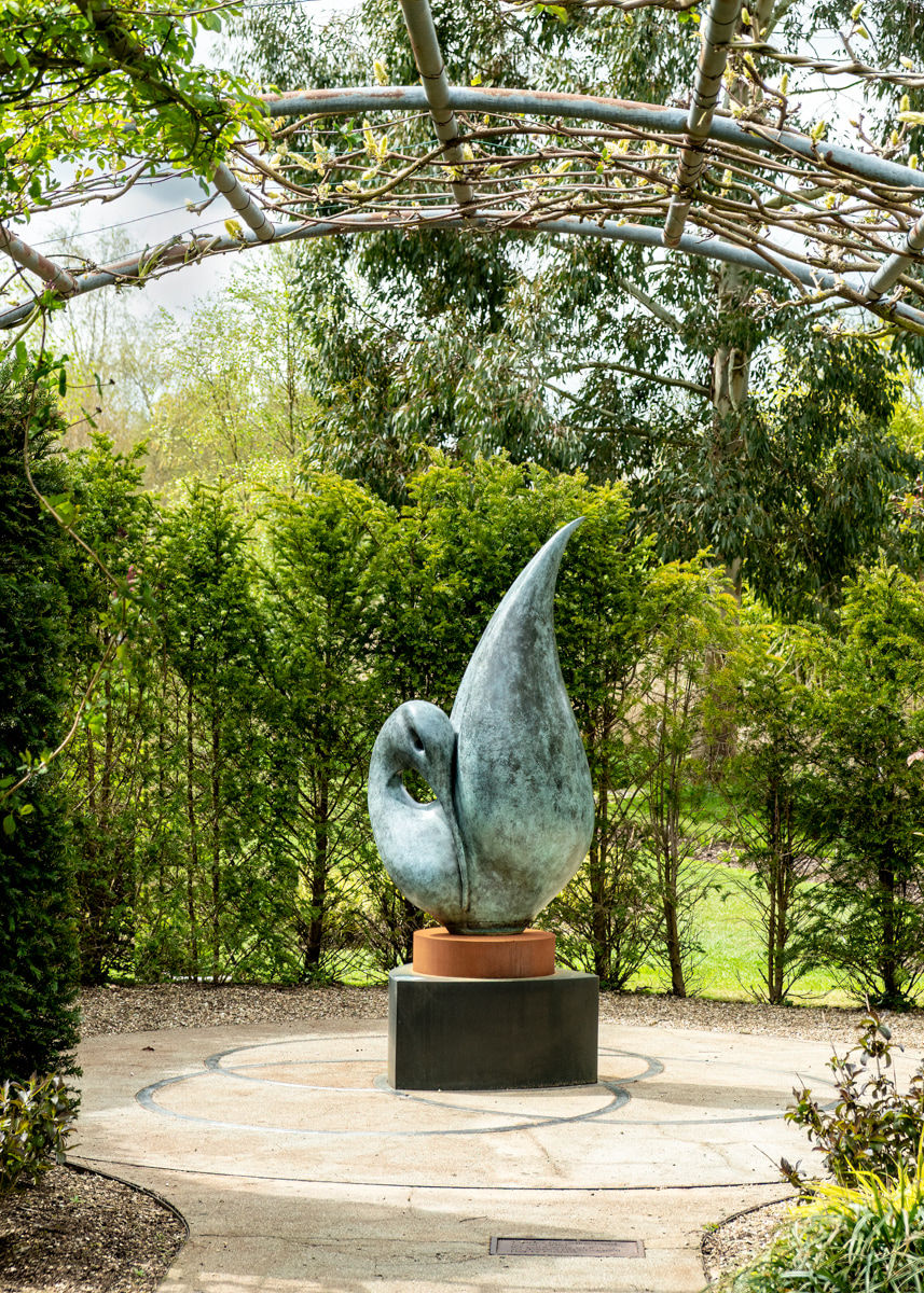Simon Gudgeon bronze sculpture Reflection featuring an elegant abstract organic form with sweeping curved bronze surfaces displayed within a landscaped outdoor setting.
