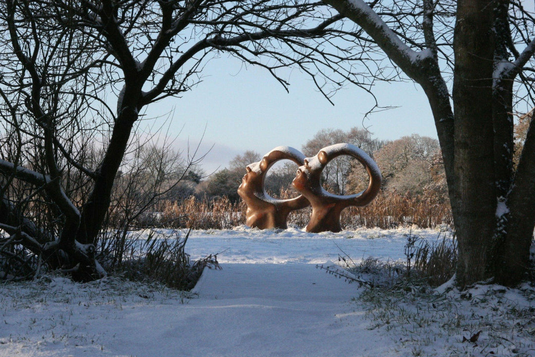 Simon Gudgeon bronze sculpture Search for Enlightenment featuring monumental interlocking abstract human forms with circular openings displayed within a landscaped outdoor setting.