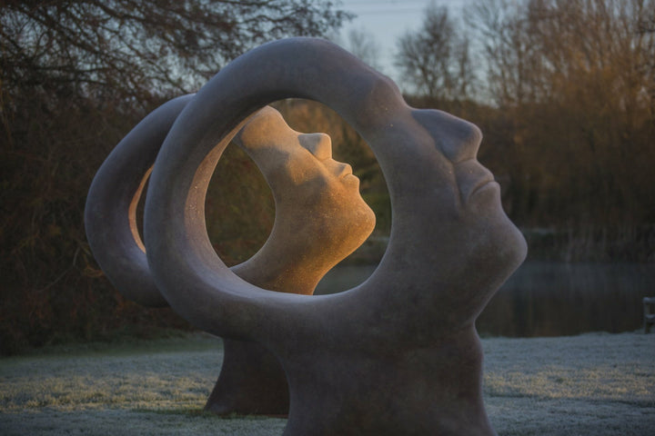 Simon Gudgeon bronze sculpture Search for Enlightenment featuring monumental interlocking abstract human forms with circular openings displayed within a landscaped outdoor setting.