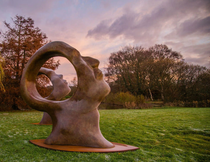 Simon Gudgeon bronze sculpture Search for Enlightenment featuring monumental interlocking abstract human forms with circular openings displayed within a landscaped outdoor setting.