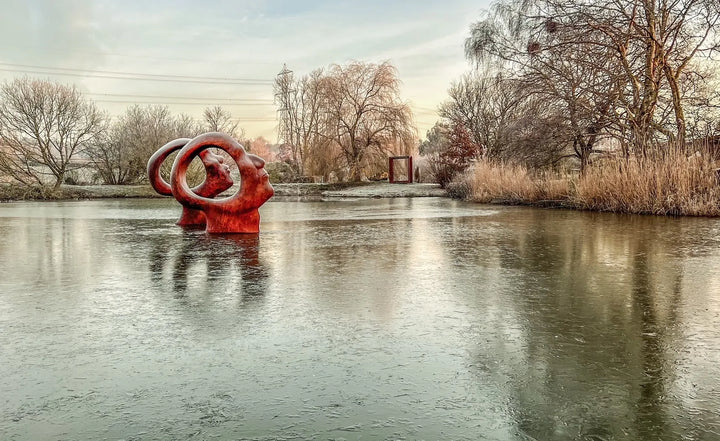 Simon Gudgeon bronze sculpture Search for Enlightenment featuring monumental interlocking abstract human forms with circular openings displayed within a landscaped outdoor setting.