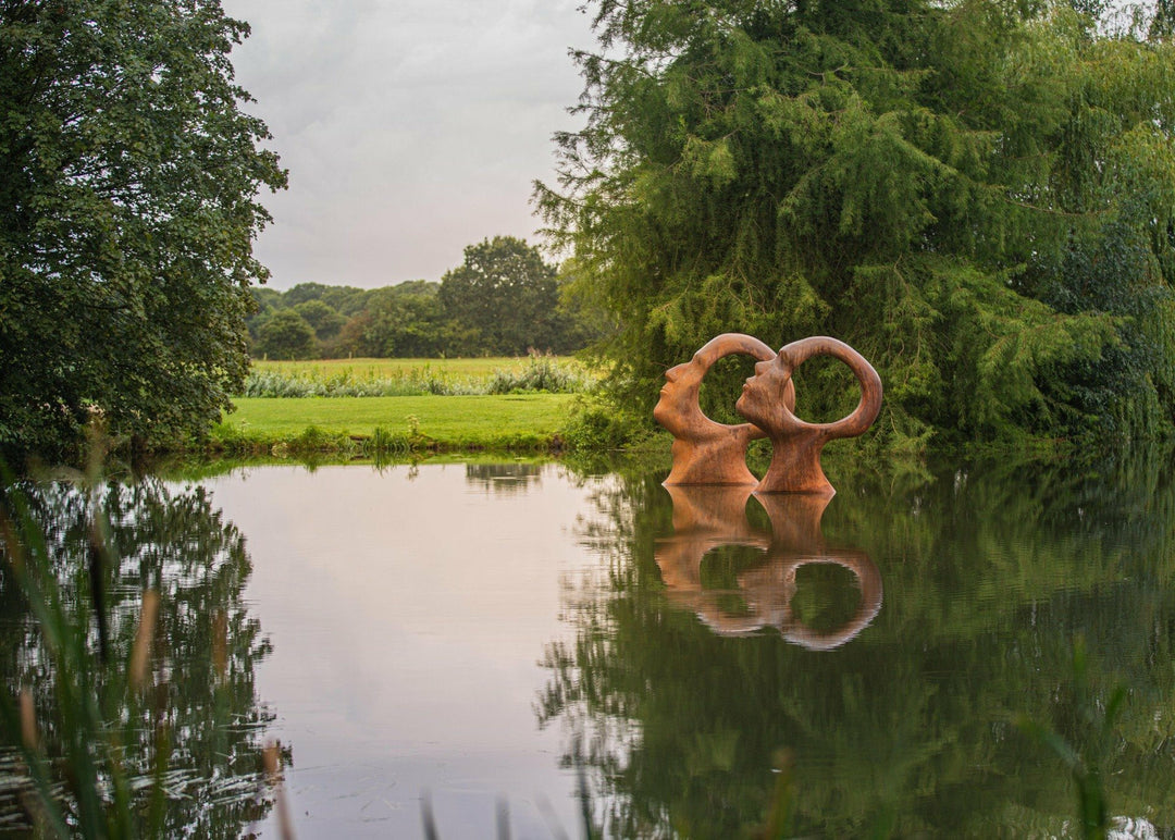 Simon Gudgeon bronze sculpture Search for Enlightenment featuring monumental interlocking abstract human forms with circular openings displayed within a landscaped outdoor setting.