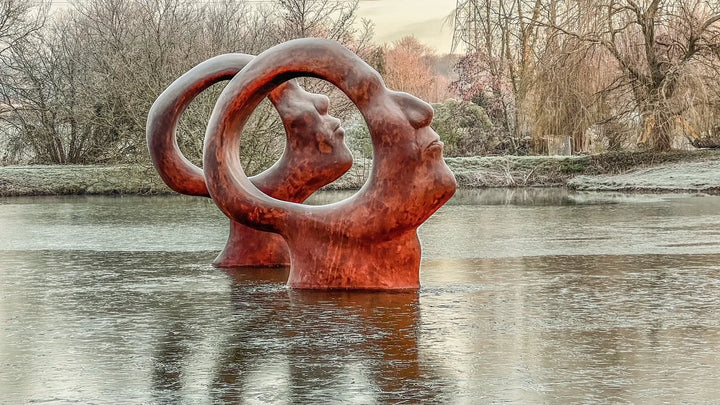 Simon Gudgeon bronze sculpture Search for Enlightenment featuring monumental interlocking abstract human forms with circular openings displayed within a landscaped outdoor setting.