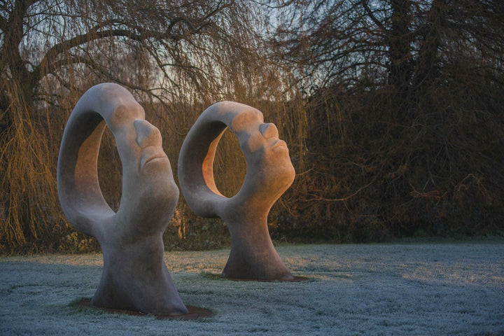Simon Gudgeon bronze sculpture Search for Enlightenment featuring monumental interlocking abstract human forms with circular openings displayed within a landscaped outdoor setting.