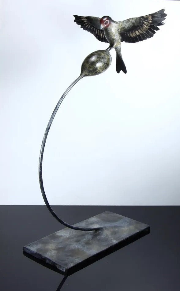 ‘Thistle Tweaker’ by Pat Bull, a limited-edition contemporary bronze wildlife sculpture depicting a goldfinch landing on a rounded teasel head with its wings fully outstretched. The bird features individually detailed bronze feathers, a distinctive reddish-brown face, dark wings with subtle bronze highlights and a forked tail. The teasel head is supported by a slender, sweeping curved steel stem rising from a rectangular bronze base, with dark grey, charcoal and muted green patina tones creating an elegant 