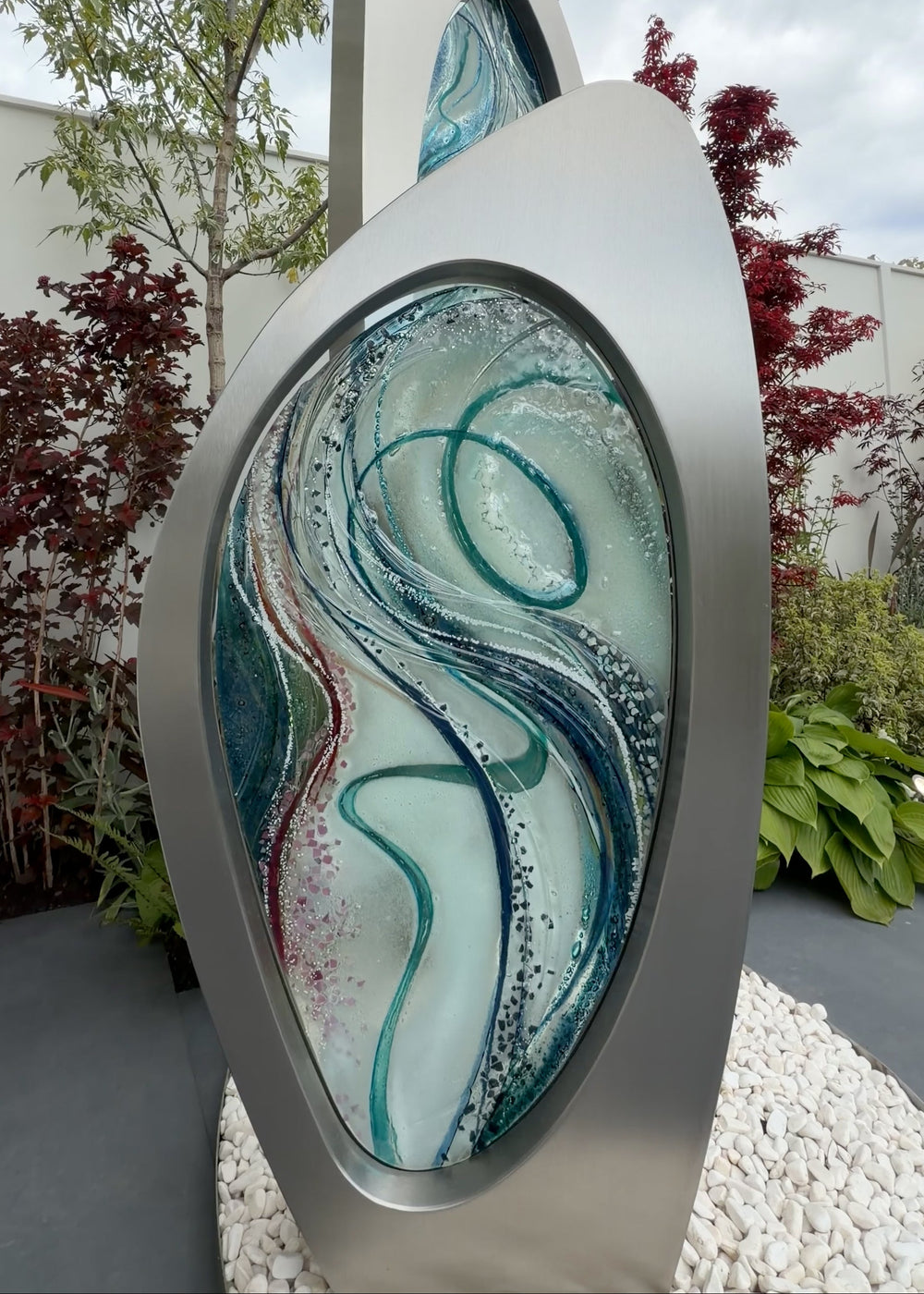 Double Apogee by Carrie-Anne Funnell, a large contemporary outdoor sculpture comprising two sweeping brushed stainless-steel forms inset with layered turquoise, blue and green kiln-formed glass.