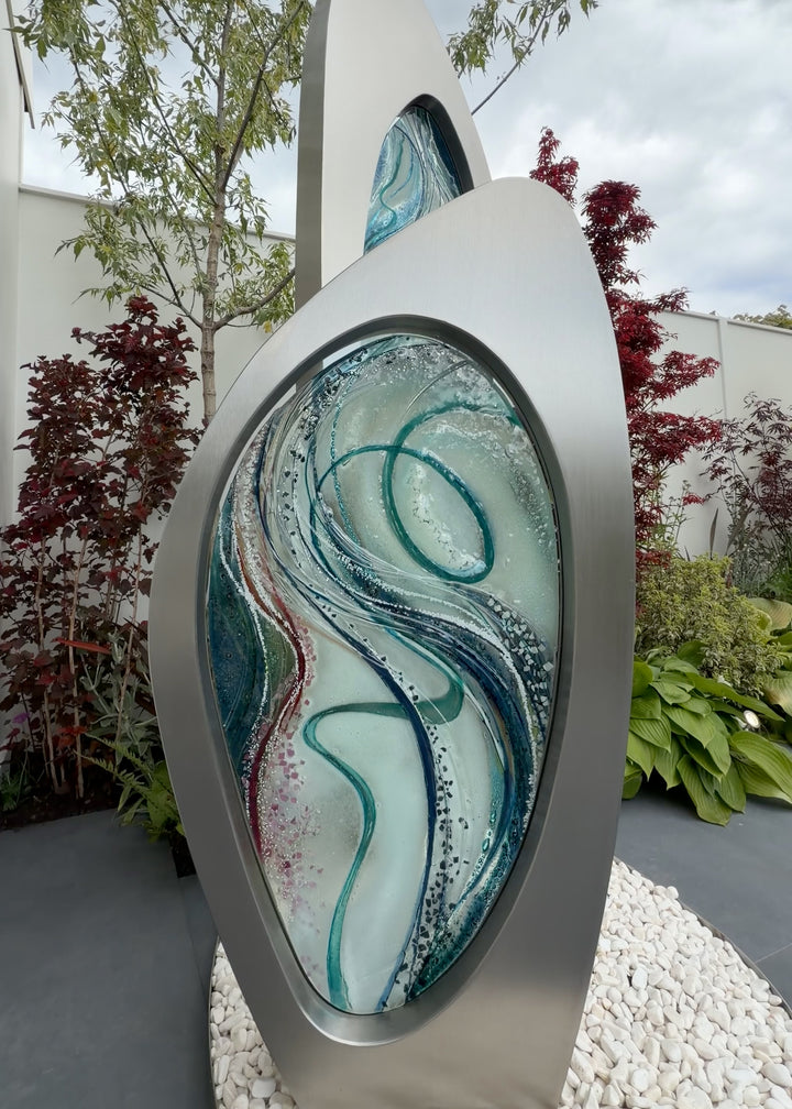 Double Apogee by Carrie-Anne Funnell, a large contemporary outdoor sculpture comprising two sweeping brushed stainless-steel forms inset with layered turquoise, blue and green kiln-formed glass.