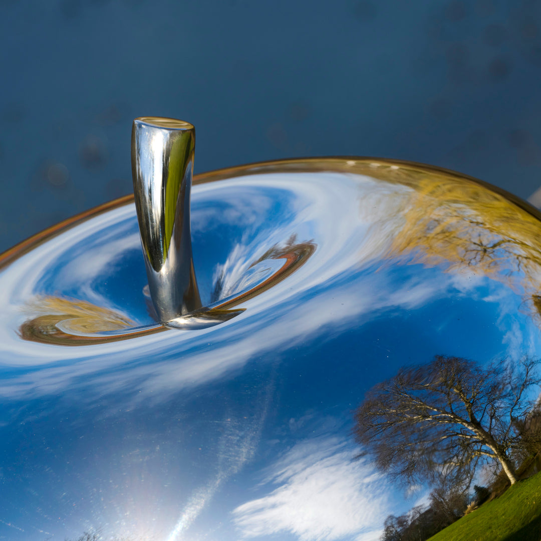 Mirror-polished stainless steel apple sculpture by James Parker, with a smooth reflective surface and softly rounded sculptural form.