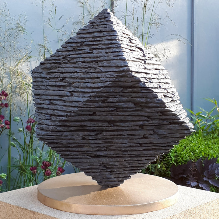 Bronze Cube sculpture by James Parker, balanced on one corner with a layered stacked-slate texture and precise geometric form.