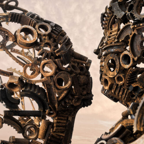 Blown Away by Penny Hardy — a striking figurative sculpture composed of welded reclaimed metal components, depicting two intertwined human forms dissolving into windblown fragments, captured against an open landscape and soft sky.