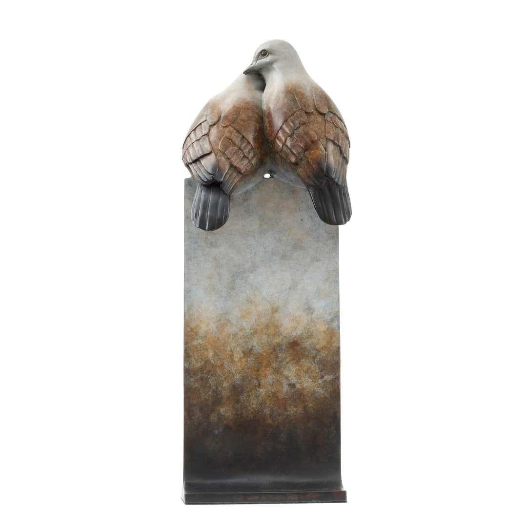 ‘Only Love’ by Pat Bull, a limited-edition contemporary bronze wildlife sculpture depicting two turtle doves perched closely together, their heads gently touching in an affectionate pose. The birds feature rounded bodies, delicate facial details and finely textured feathers in warm brown, soft grey, cream and pale bronze tones. Mounted on a tall rectangular bronze pedestal, the sculpture features a waxed, mottled patina fading from pale ivory and grey through earthy brown to dark charcoal and black, present