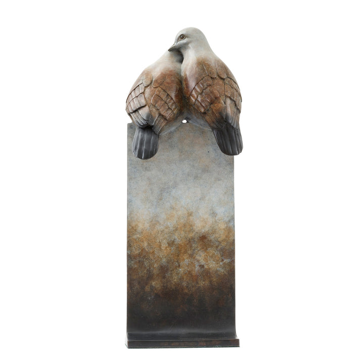 ‘Only Love’ by Pat Bull, a limited-edition contemporary bronze wildlife sculpture depicting two turtle doves perched closely together, their heads gently touching in an affectionate pose. The birds feature rounded bodies, delicate facial details and finely textured feathers in warm brown, soft grey, cream and pale bronze tones. Mounted on a tall rectangular bronze pedestal, the sculpture features a waxed, mottled patina fading from pale ivory and grey through earthy brown to dark charcoal and black, present