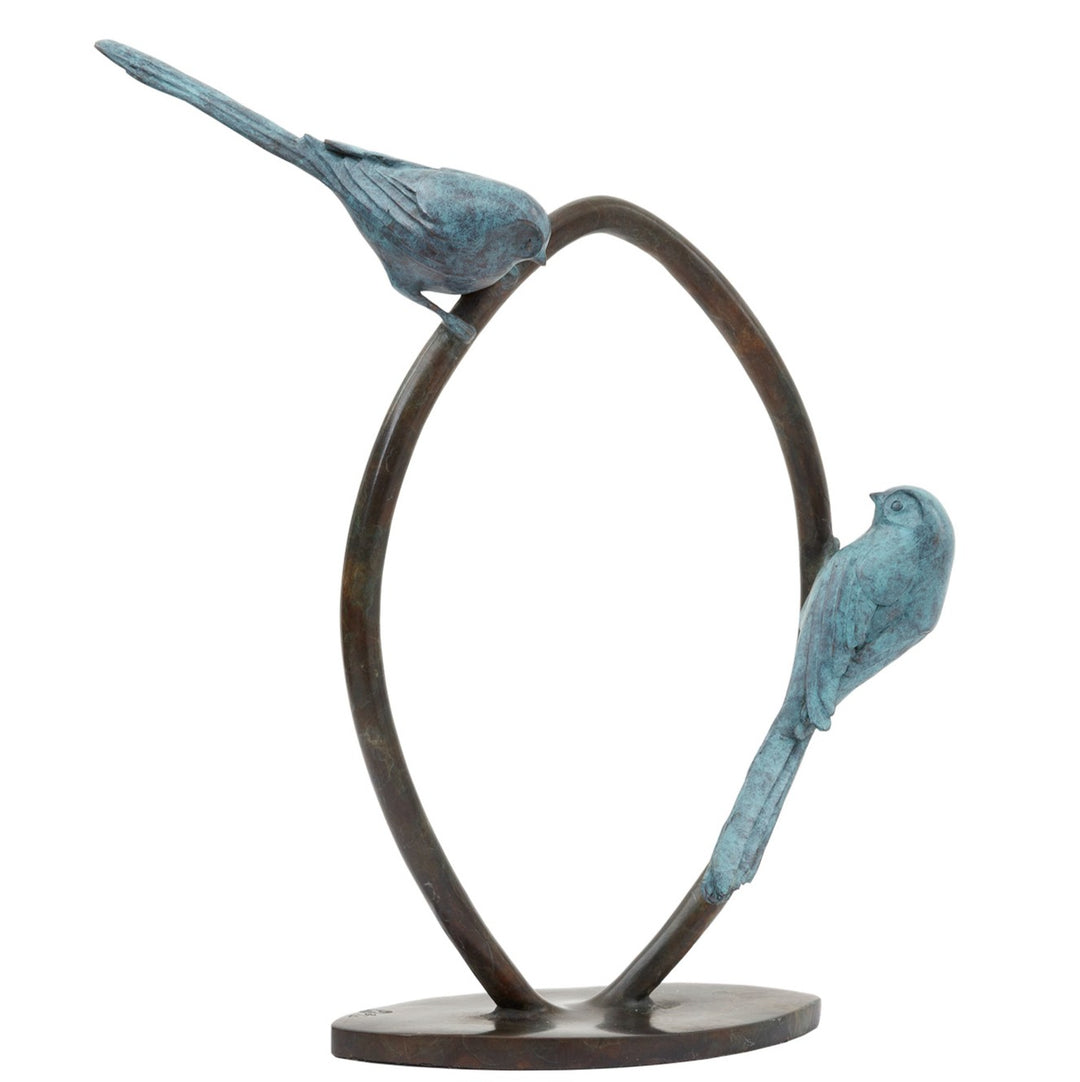 ‘Two’s Company’ by Pat Bull, a limited-edition contemporary bronze wildlife sculpture depicting two long-tailed tits perched on opposite sides of an upright circular bronze ring, facing towards one another. Each bird features a small rounded body, delicate beak, finely textured feathers and an elongated tail, finished in soft turquoise, teal and blue-green verdigris patina. The birds contrast with the dark brown and warm bronze tones of the open ring, which stands on a low oval bronze base against a white b
