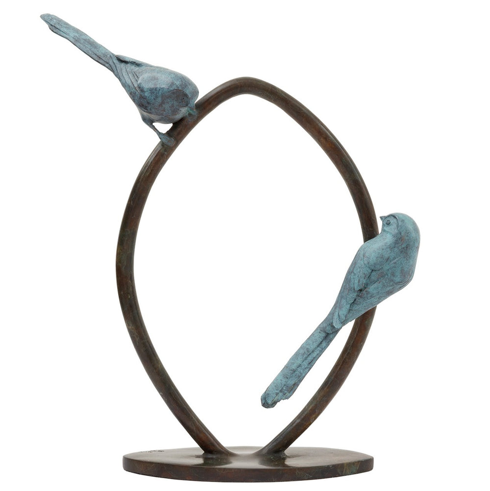 ‘Two’s Company’ by Pat Bull, a limited-edition contemporary bronze wildlife sculpture depicting two long-tailed tits perched on opposite sides of an upright circular bronze ring, facing towards one another. Each bird features a small rounded body, delicate beak, finely textured feathers and an elongated tail, finished in soft turquoise, teal and blue-green verdigris patina. The birds contrast with the dark brown and warm bronze tones of the open ring, which stands on a low oval bronze base against a white b