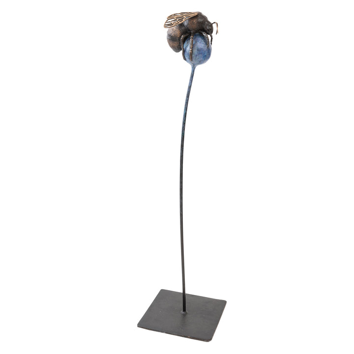 ‘The Bee All and End All’ by Pat Bull, a limited-edition contemporary bronze wildlife sculpture depicting an oversized bumblebee resting on a rounded abstract flower head. The bee features a textured body in dark brown and warm bronze tones, delicate bronze antennae, six detailed legs and intricate openwork wings with polished golden highlights. The spherical flower head is finished in mottled blue, purple and violet patina, supported by a tall, slender steel stem rising from a square dark metal base.