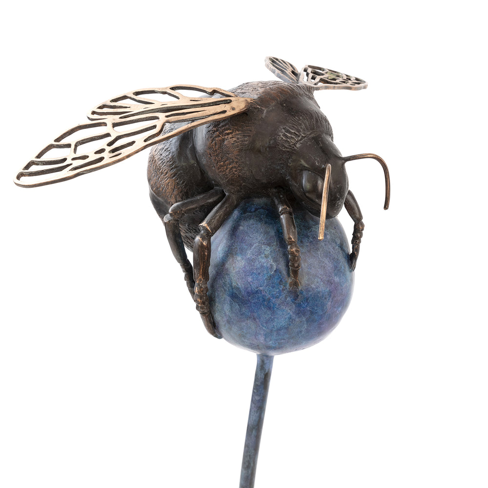 ‘The Bee All and End All’ by Pat Bull, a limited-edition contemporary bronze wildlife sculpture depicting an oversized bumblebee resting on a rounded abstract flower head. The bee features a textured body in dark brown and warm bronze tones, delicate bronze antennae, six detailed legs and intricate openwork wings with polished golden highlights. The spherical flower head is finished in mottled blue, purple and violet patina, supported by a tall, slender steel stem rising from a square dark metal base.