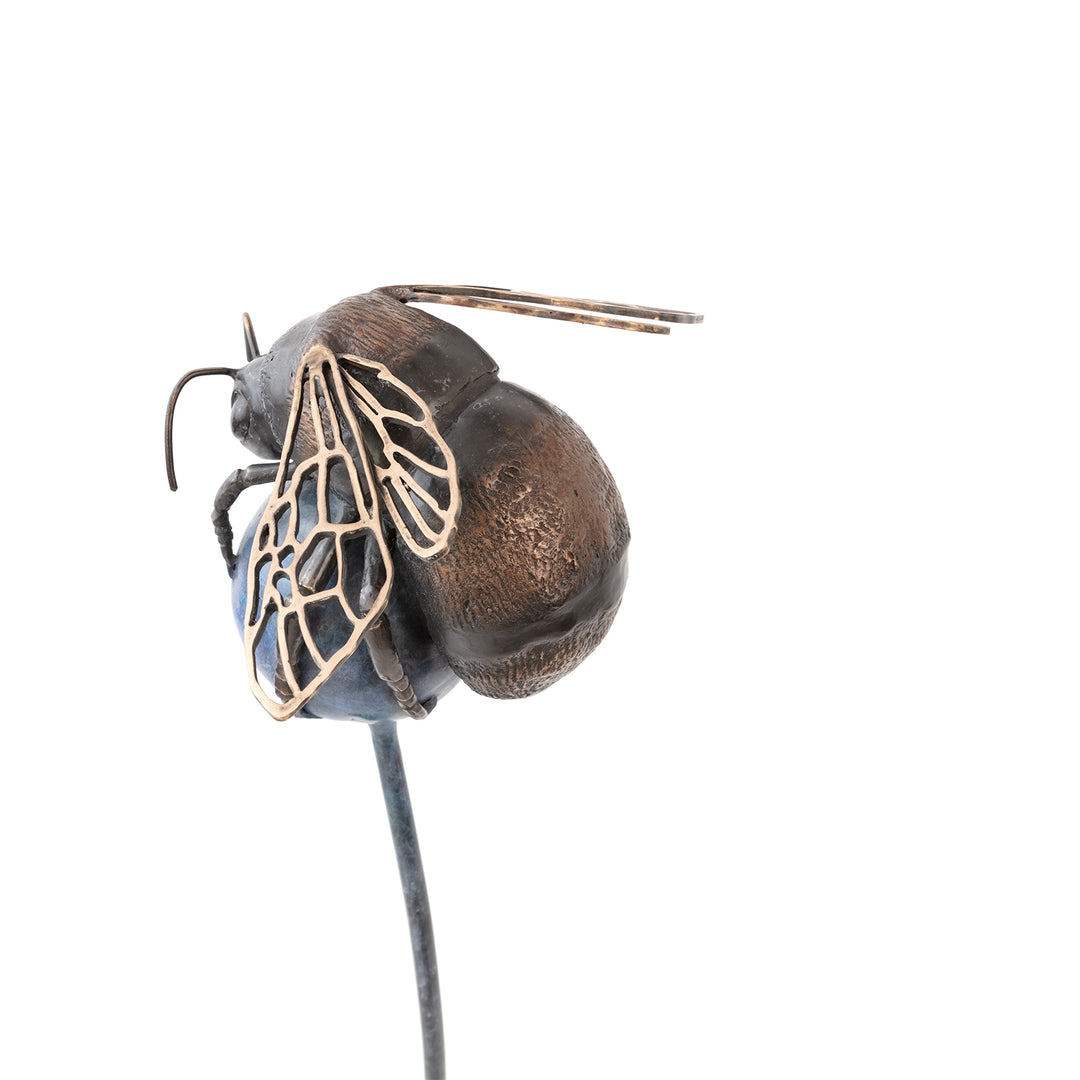 ‘The Bee All and End All’ by Pat Bull, a limited-edition contemporary bronze wildlife sculpture depicting an oversized bumblebee resting on a rounded abstract flower head. The bee features a textured body in dark brown and warm bronze tones, delicate bronze antennae, six detailed legs and intricate openwork wings with polished golden highlights. The spherical flower head is finished in mottled blue, purple and violet patina, supported by a tall, slender steel stem rising from a square dark metal base.