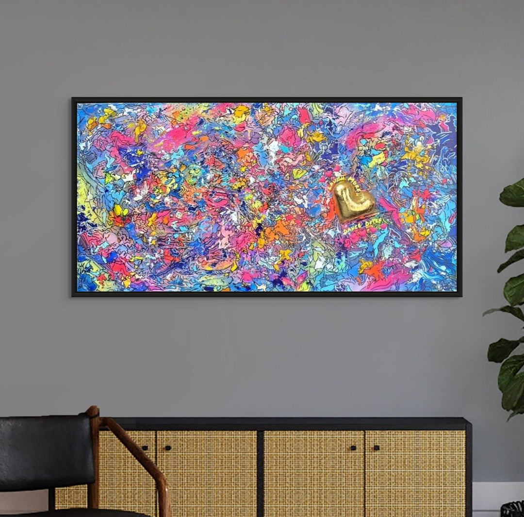 A vibrant abstract mixed-media painting bursting with swirling colours in pink, blue, yellow, orange and purple, with heavy texture and fluid forms. At the right side, a raised gold 3D heart sits prominently with text around it reading “Laugh More, Dance Often”. The artwork has an expressive, energetic surface with layered paint and resin details.