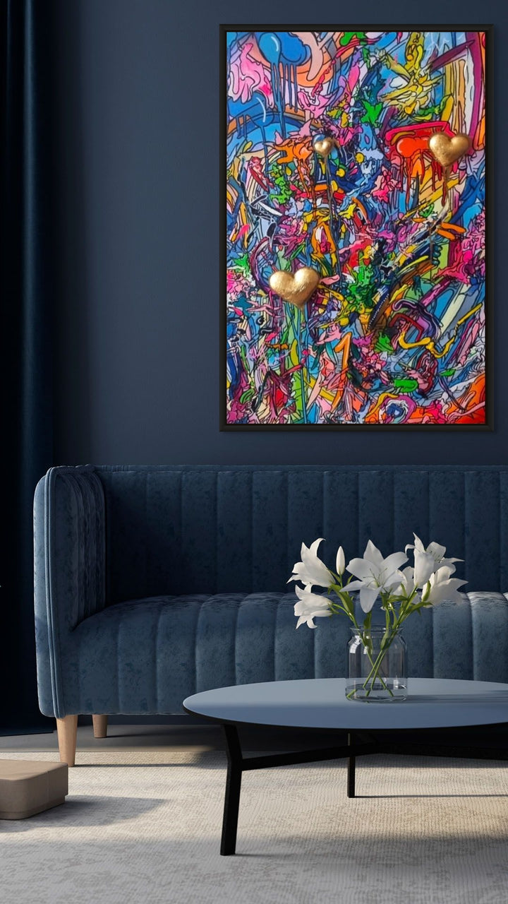 A vibrant mixed-media abstract artwork filled with layered graffiti-style lines, drips and splashes in bright pinks, blues, yellows and greens, featuring three raised gold 3D heart elements floating within the composition, framed in a black tray frame.