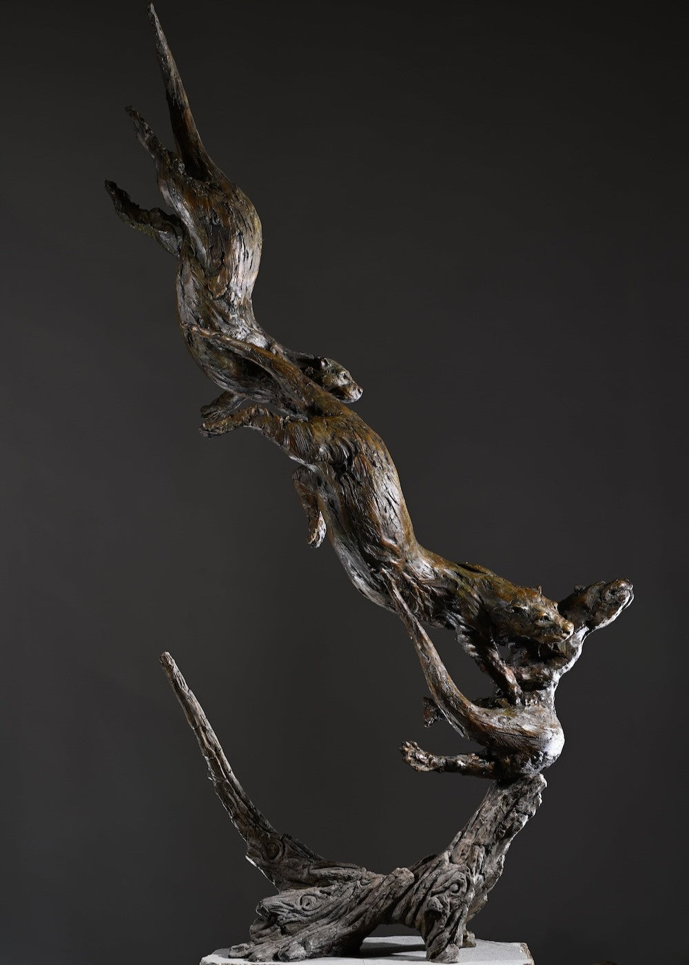 ‘Otters Playing Underwater’ by Hamish Mackie, a life-size limited-edition bronze wildlife sculpture depicting a mother otter and her playful cubs twisting, diving and swimming around a sculpted underwater tree root. The dynamic vertical composition features expressive animal movements, detailed fur textures and a weathered bronze finish in rich brown and earthy tones, capturing the playful energy and natural behaviour of otters beneath the water.