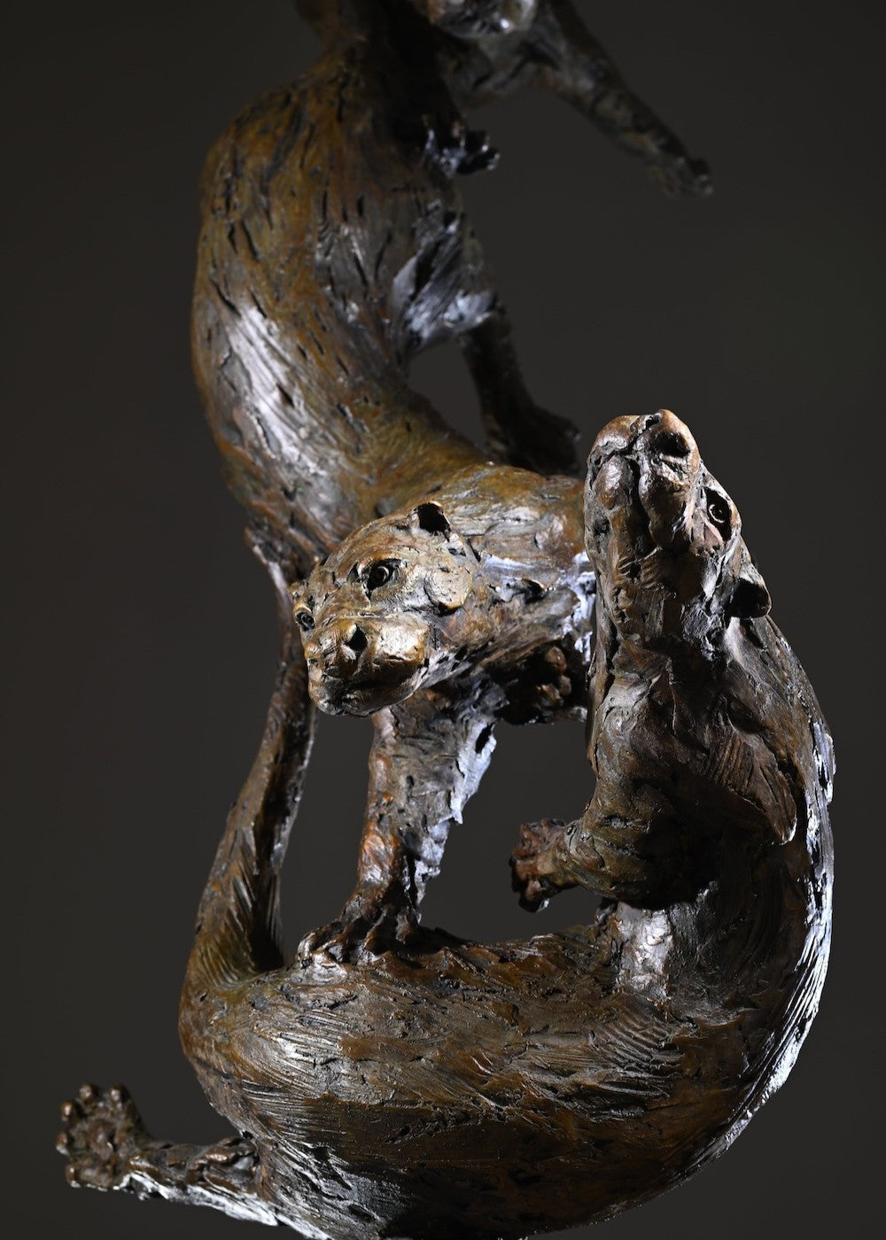 ‘Otters Playing Underwater’ by Hamish Mackie, a life-size limited-edition bronze wildlife sculpture depicting a mother otter and her playful cubs twisting, diving and swimming around a sculpted underwater tree root. The dynamic vertical composition features expressive animal movements, detailed fur textures and a weathered bronze finish in rich brown and earthy tones, capturing the playful energy and natural behaviour of otters beneath the water.