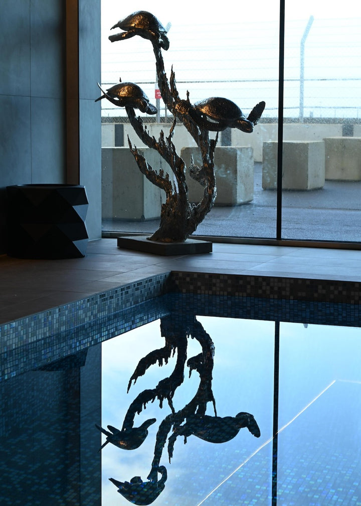 ‘Turtles Stainless Steel’ by Hamish Mackie, a limited-edition marine-grade stainless steel wildlife sculpture depicting three life-size sea turtles swimming through an intricate arrangement of underwater foliage. The polished silver-grey finish highlights the turtles' detailed shells, textured flippers and graceful movement, while the sweeping, branching forms create a sense of flowing water. Mounted on a rectangular stainless steel base, this contemporary sculpture is suitable for indoor or outdoor display