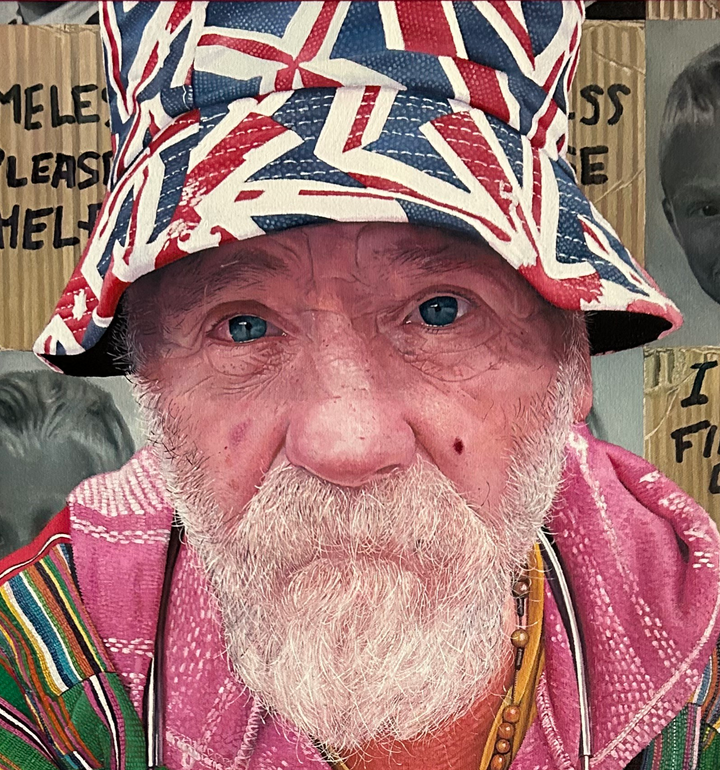 Mick by James Earley — a hyperrealist oil painting of an elderly homeless man in a colourful patchwork jacket and Union Jack bucket hat, staring directly at the viewer with blue eyes full of depth and resilience, his knuckles spelling “LOVE.” Behind him, cardboard signs and childhood photos evoke themes of loss, survival, and invisible trauma.